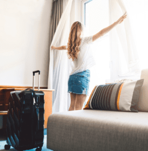 Frau vor Hotel Fenster mit frisch gereinigten Gardinen aus der Gardinenreinigung.